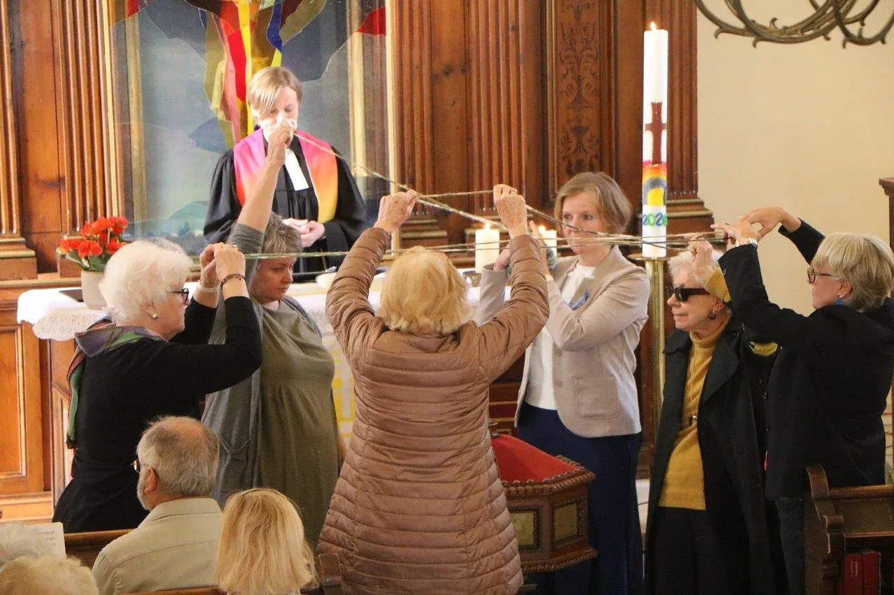 Frauen stehen im Kreis und spamnnen ein Netz zwichen sich auf