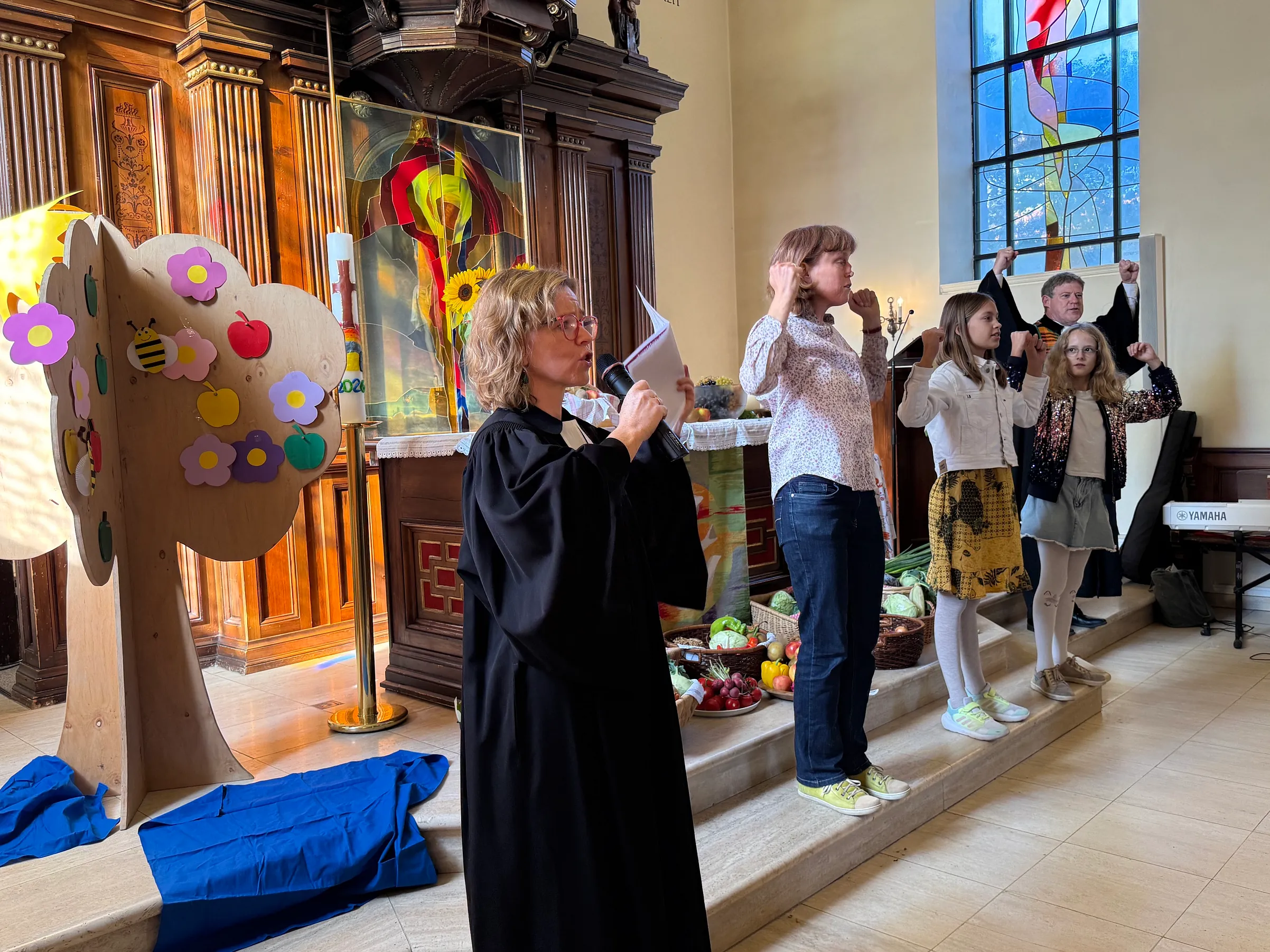 Vikarin, Gemeindepädagogin, Kinder und Pfarrer stehen mit erhobenen Händen vor einem Altar